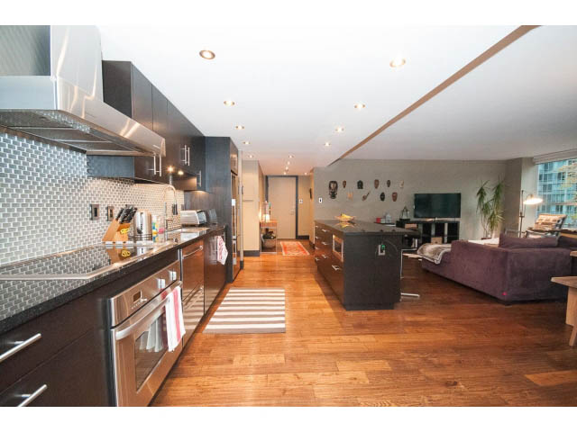 Bright kitchen with stainless steel appliances and dark wood cabinets, open to a spacious living area with hardwood...