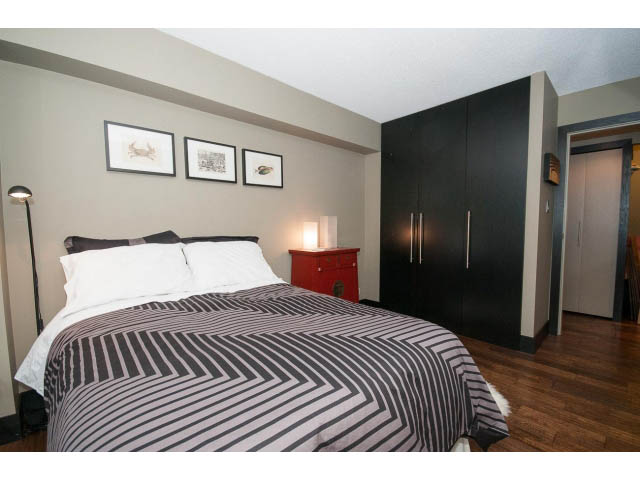 Furnished bedroom with striped bedding, dark cabinets, and hardwood floors. - 303 - 717 Jervis St, Vancouver Downtown
