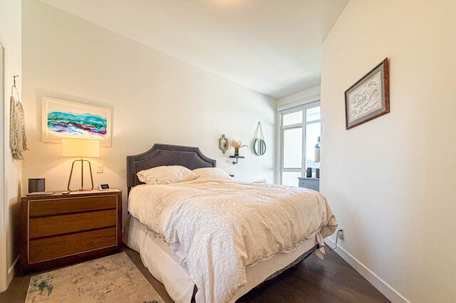 Bedroom with gray upholstered headboard, white bedding, and dark hardwood floors. - 503-105 West 2nd Street, North Vancouver