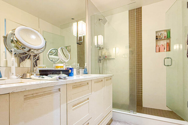 Bathroom with white marble countertops, cream cabinetry, and a glass-enclosed walk-in shower with mosaic tile accents.