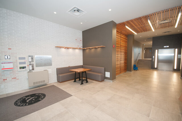 Spacious condo lobby with white brick wall, wood slat ceiling, and built-in bench seating around a wooden table.