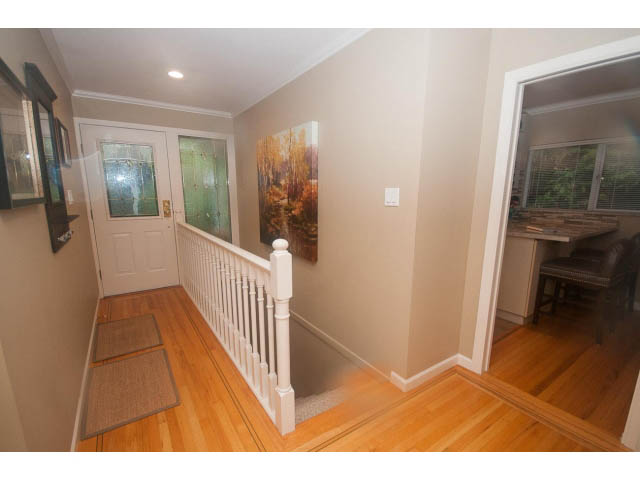Bright entryway with hardwood floors and a white railing leading to the stairs. - 8135 Pasco Rd, West Vancouver