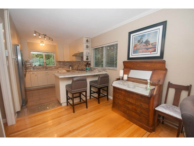 Open-concept living area with hardwood floors, kitchen counters, and framed artwork. - 8135 Pasco Rd, West Vancouver
