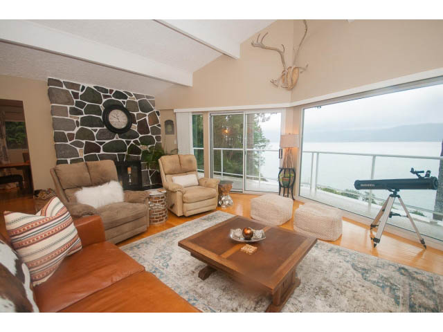 Spacious living room with large windows, stone accent wall, and waterfront view. - 8135 Pasco Rd, West Vancouver
