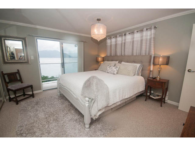 Spacious bedroom with a cozy bed, large windows, and a view of the water. - 8135 Pasco Rd, West Vancouver