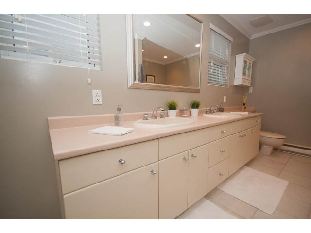 Bright bathroom with dual sinks, beige cabinets, and a large mirror. - 8135 Pasco Rd, West Vancouver