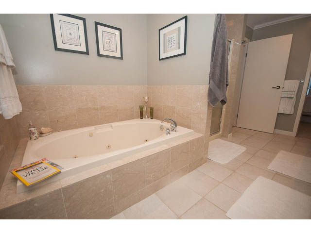 Spacious bathroom with beige tiles and a bathtub, featuring framed artwork on the wall. - 8135 Pasco Rd, West Vancouver