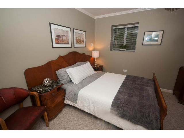Furnished bedroom with wooden headboard, gray bedding, and framed artwork. - 8135 Pasco Rd, West Vancouver