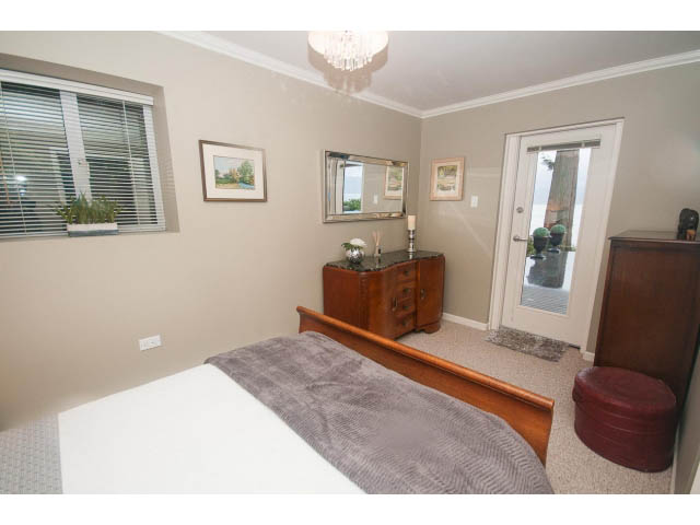 Furnished bedroom with wooden furniture, large mirror, and window with blinds. - 8135 Pasco Rd, West Vancouver
