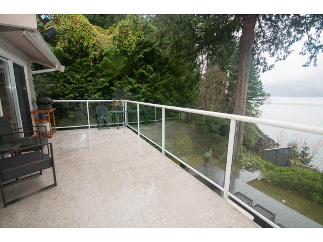 Furnished patio with glass railings, overlooking a serene lake and lush greenery. - 8135 Pasco Rd, West Vancouver