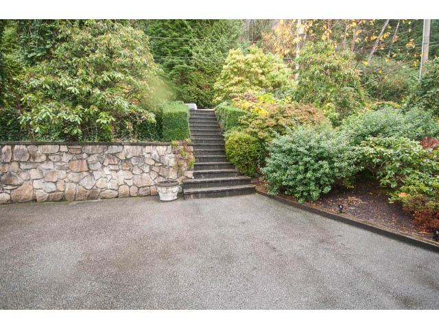 Staircase leading to lush garden, stone wall, and concrete driveway. - 8135 Pasco Rd, West Vancouver