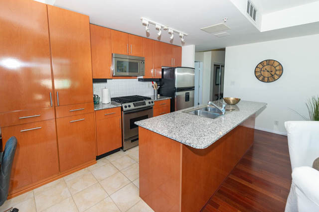 Bright kitchen with granite countertops and wooden cabinets, open to a living area with hardwood floors.