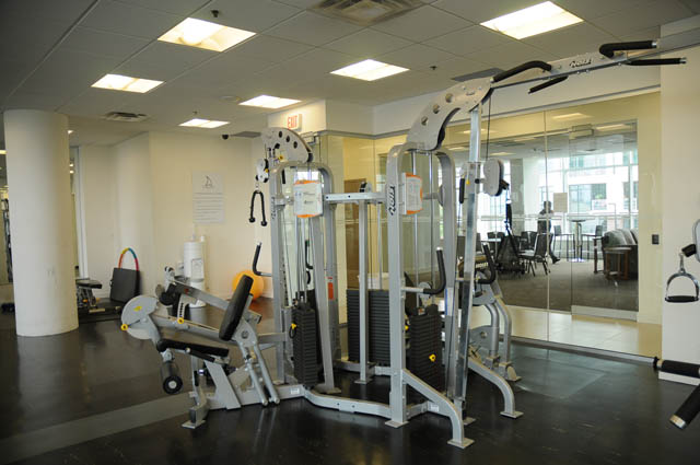 Bright gym with mirrored walls and weight machines, city view through windows. - 1905 - 138 East Esplanade Ave, North Vancouver