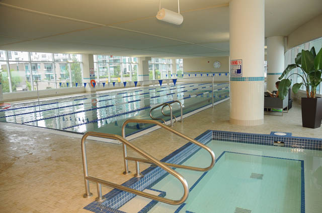 Spacious indoor pool with tiled floors and railings, city view in background. - 1905 - 138 East Esplanade Ave, North Vancouver