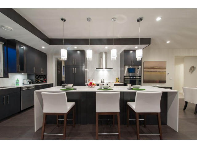 Bright kitchen with modern white and black cabinetry, hardwood floors, and a central island. - 3192 Beverley Cres, North Vancouver