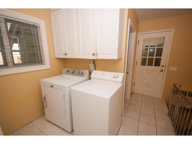 Bright laundry room with white cabinets, tiled floor, and window view. - 1145 Sutton Place, West Vancouver