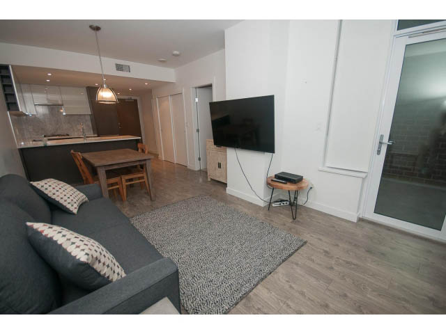 Bright living room with modern decor, hardwood floors, and a flat-screen TV. - 203 - 110 Switchmen St, Vancouver East Side