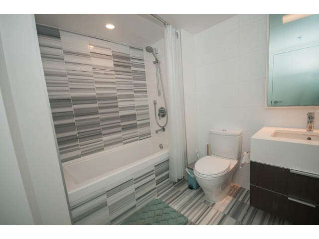 Furnished 1-bedroom condo with modern bathroom, white tiles, and a sleek vanity. - 203 - 110 Switchmen St, Vancouver East Side