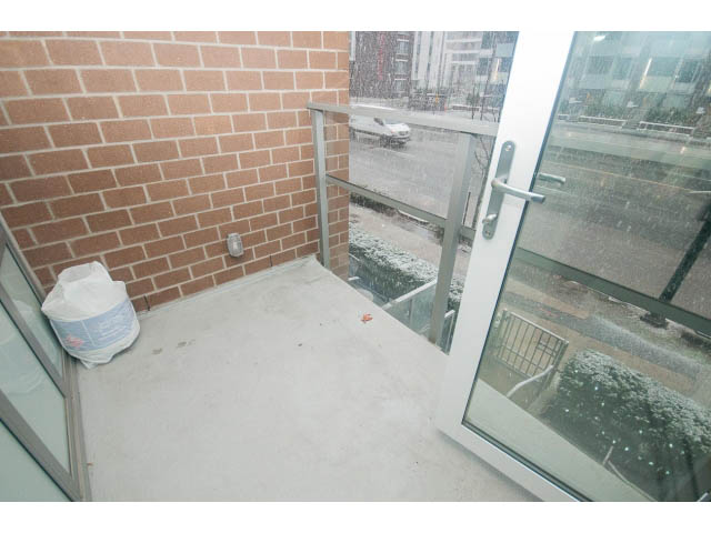 Bright balcony with brick wall and glass door, snow-covered ground visible. - 203 - 110 Switchmen St, Vancouver East Side