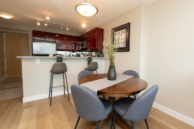 Modern dining area with wooden table, gray upholstered chairs, and red kitchen cabinets. - 2303 - 1328 West Pender Street, Vancouver Downtown