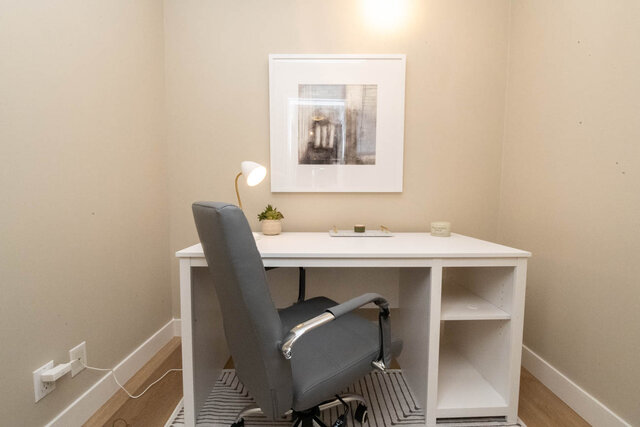 Compact home office with a white desk, gray chair, and framed artwork, perfect for a cozy workspace.
