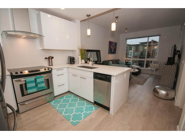 Bright kitchen with white cabinets and hardwood floors, leading to a cozy living area with a city view. - 416 - 733 West 3rd St, North Vancouver