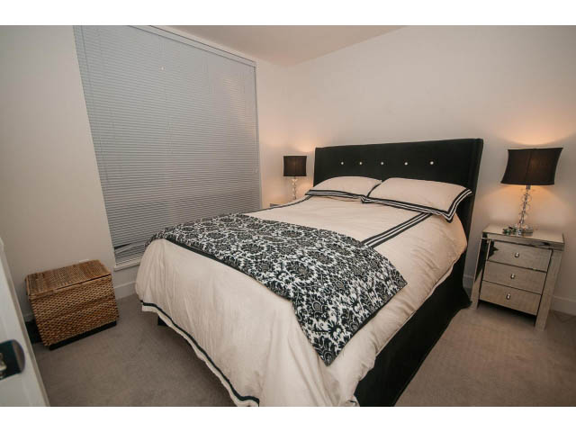 Furnished 1-bedroom + den with black and white bedding, nightstands, and a window with blinds. - 416 - 733 West 3rd St, North Vancouver