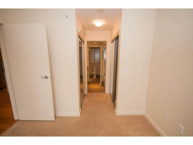 Bright hallway with light wood flooring and white walls leading to a kitchen area. - 407 - 683 Victoria Park West, North Vancouver