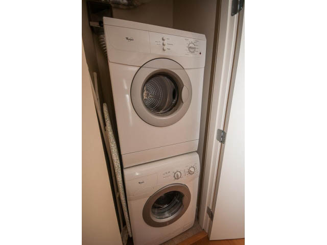 Bright laundry room with stacked washer and dryer, neutral tones. - 407 - 683 Victoria Park West, North Vancouver