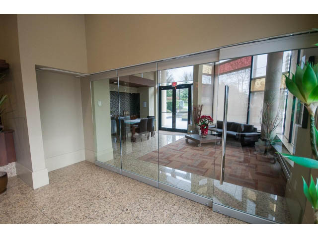 Furnished living room with glass sliding doors, modern decor, and city view. - 407 - 683 Victoria Park West, North Vancouver