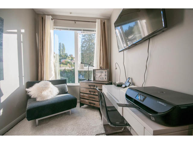 Bright living room with city view, modern furniture, and a flat-screen TV mounted on the wall. - 203 - 3825 Cate's Landing, North Vancouver