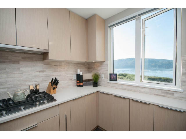 Bright kitchen with light wood cabinets, white countertops, and a stunning ocean view through large windows.
