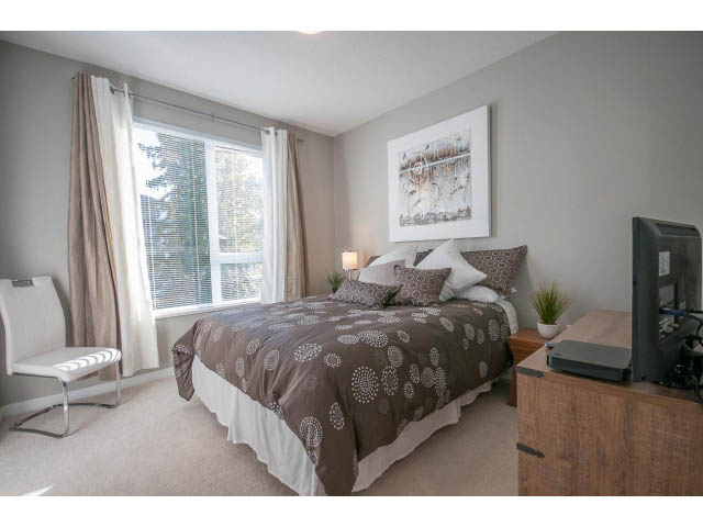 Furnished bedroom with large bed, patterned bedding, and a desk with chair. - 203 - 3825 Cate's Landing, North Vancouver