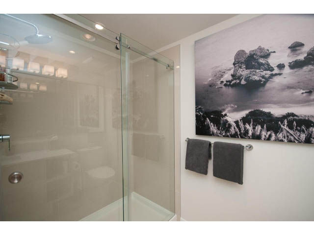 Bright bathroom with glass shower and coastal artwork. - 203 - 3825 Cate's Landing, North Vancouver