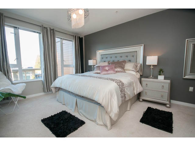 Spacious bedroom with gray walls, tufted headboard, and large windows. - 203 - 3825 Cate's Landing, North Vancouver