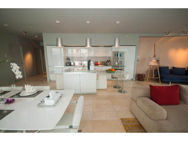 Bright kitchen with white countertops and modern pendant lights, seamlessly connected to a cozy living area with a beige...