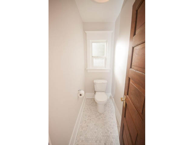 Bright bathroom with white walls, mosaic tile floor, and wooden cabinets. - 516 E 10th Ave, Vancouver East Side