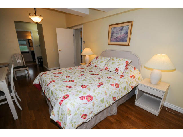 Spacious bedroom with floral bedding, hardwood floors, and a desk area. - 1397 Tatlow Avenue, North Vancouver