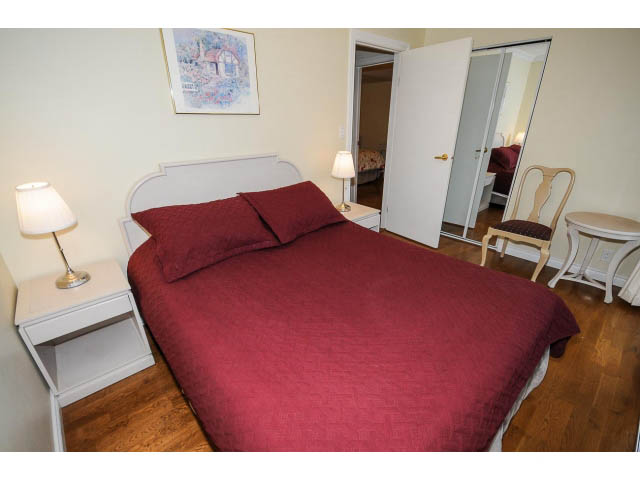 Furnished bedroom with hardwood floors, red bedding, and a white headboard. - 1397 Tatlow Avenue, North Vancouver