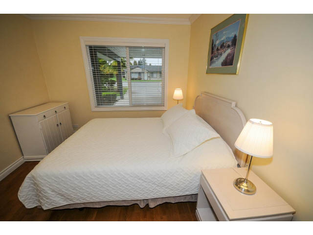 Bright bedroom with hardwood floors, white bedding, and a sliding glass door view. - 1397 Tatlow Avenue, North Vancouver