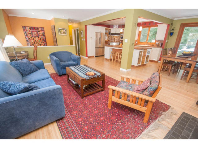 Open-concept living area with hardwood floors, a red patterned rug, and a kitchen in the background. - 2972 Wembley Dr, North Vancouver