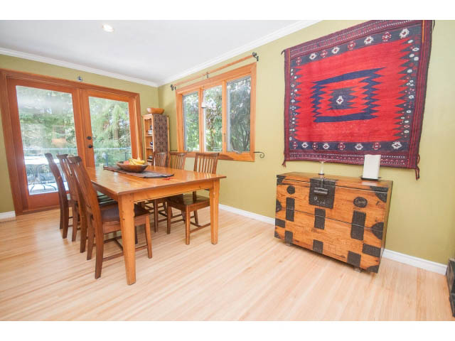 Bright dining room with hardwood floors, wooden furniture, and a vibrant red wall hanging. - 2972 Wembley Dr, North Vancouver
