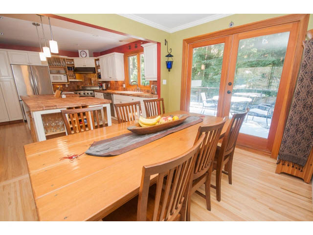 Bright dining area with wooden table, chairs, and kitchen in the background. - 2972 Wembley Dr, North Vancouver