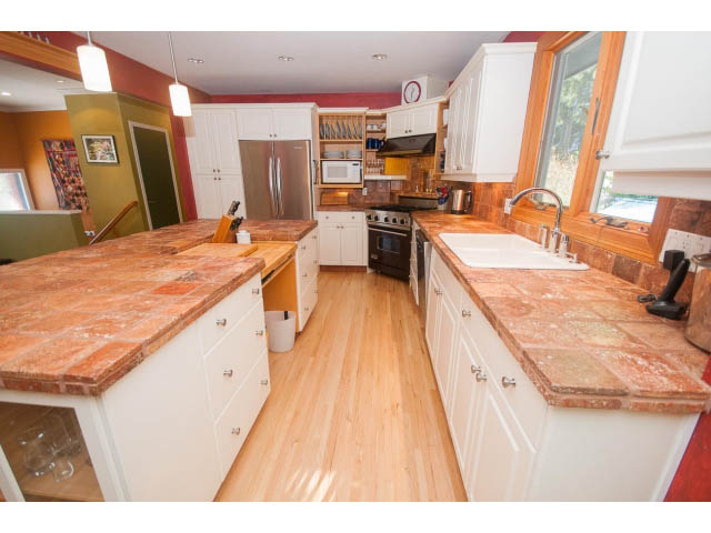 Bright kitchen with white cabinetry, terracotta countertops, and hardwood floors. - 2972 Wembley Dr, North Vancouver
