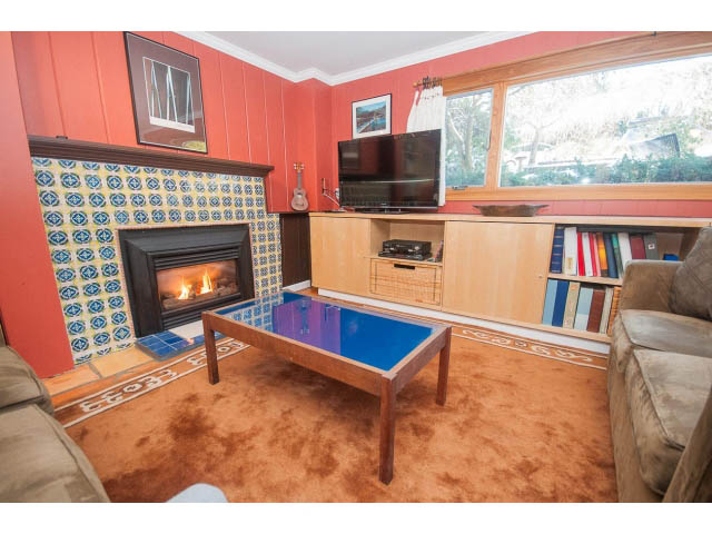 Living room with fireplace, colorful bookshelves, and large window view. - 2972 Wembley Dr, North Vancouver