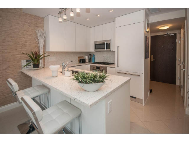 Bright kitchen with white countertops and modern appliances, featuring a cozy corner with a bar stool. - 1008-199 Victory Ship Way, North Vancouver