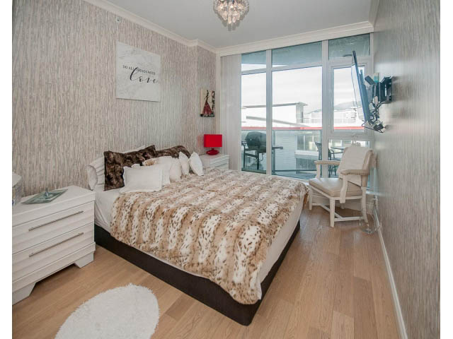 Bright bedroom with hardwood floors, city view, and a cozy bed setup. - 1008-199 Victory Ship Way, North Vancouver