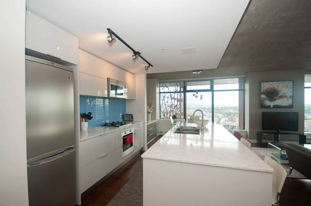 Bright kitchen with modern appliances, white countertops, and hardwood floors, featuring a city view through large windows.