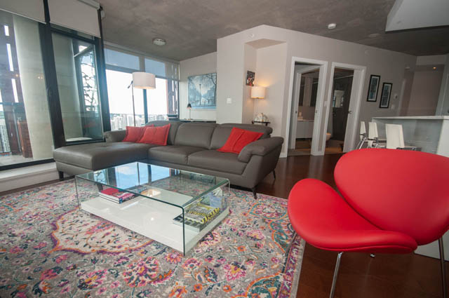 Furnished living room with a grey sectional, red chairs, and a patterned rug. - 3806 - 128 Cordova St W, Vancouver Downtown