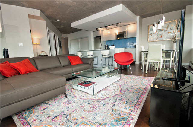 Furnished living room with modern furniture, colorful rug, and kitchen in the background. - 3806 - 128 Cordova St W, Vancouver Downtown